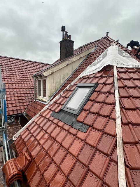 Nieuwe rode keramische dakpannen met een ingebouwd dakraam en nieuw onderdak