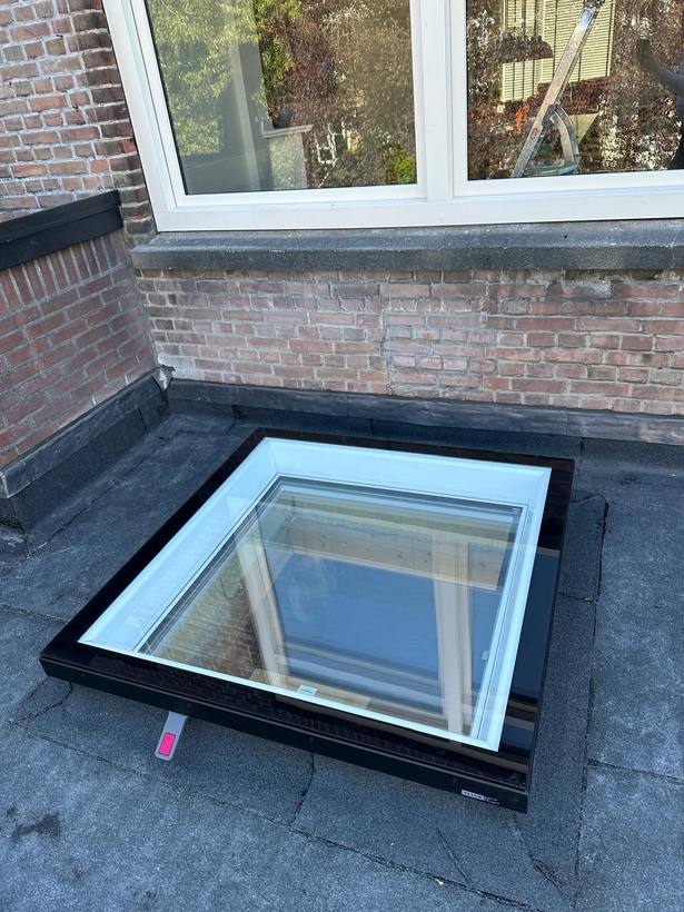 Nieuw plat dakraam geplaatst op een bitumen dak tegen de gevel